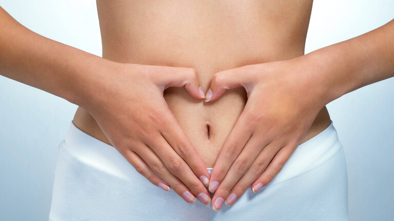 Eine Frau formt mit ihren Händen ein Herz über ihrem Bauch und Unterleib.
