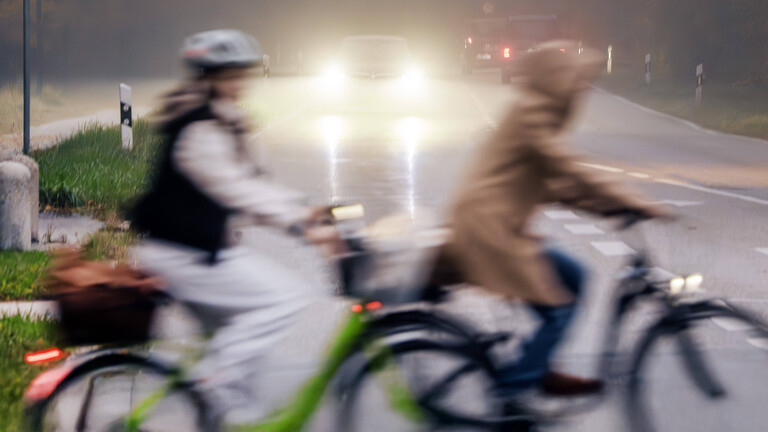 Zwei Radfahrerinnen überqueren eine vielbefahrene Landstraße