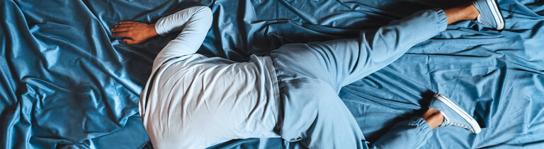 Mann liegt auf blauem Stoff, verschmilzt mit der Umgebung und drückt Traurigkeit aus, Symbolfoto