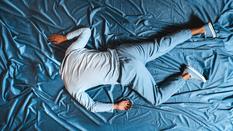 Mann liegt auf blauem Stoff, verschmilzt mit der Umgebung und drückt Traurigkeit aus, Symbolfoto