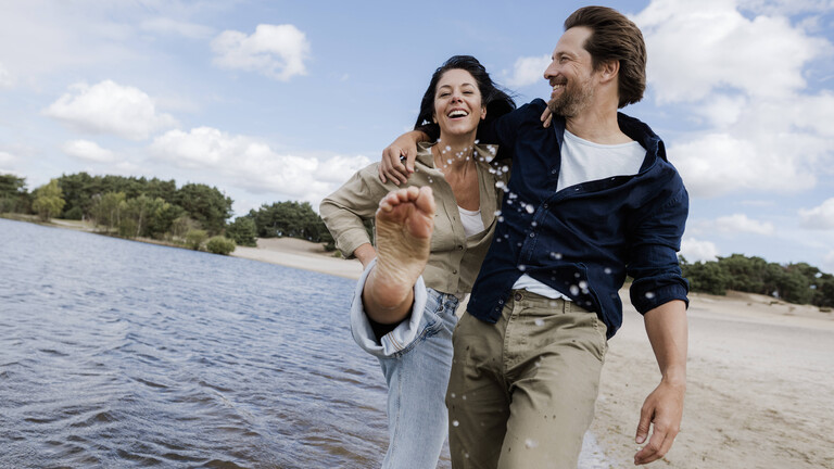 Ein Paar geht eng umschlungen an einem Strand entlang und hat Spaß dabei