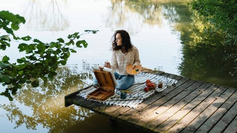 Eine Frau sitzt an einem See und malt