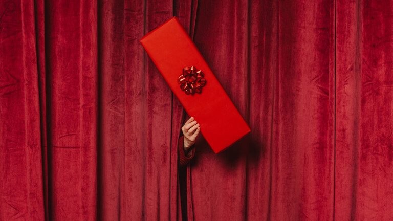 Eine Hand reicht ein Geschenk durch einen Vorhang durch