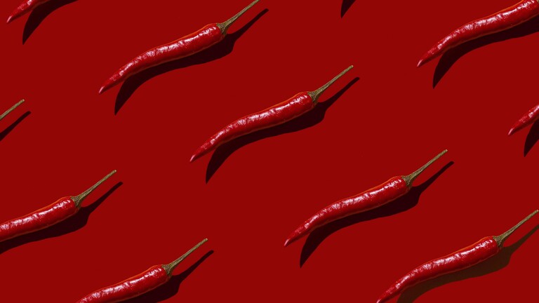 Auf einem roten Hintergrund liegen mehrere einzelne Chilischoten.