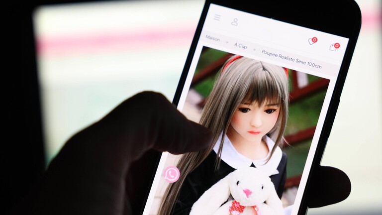 Kindliche Sexpuppen konnten über die Verkaufsplattform Shein erworben werden. Eine Person sieht sich solch eine Puppe auf einem Handydisplay an. Im Hintergrund ein beleuchteter Computerbildschirm