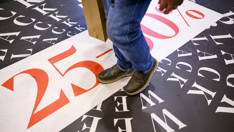 Ein Mann steht mit Einkaufstasche auf einer Werbefläche für die Black Week mit Rabattangaben.