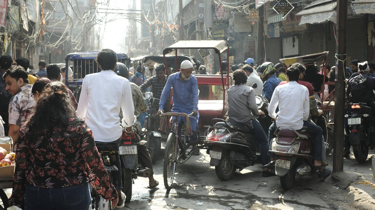 Eine Straßenszene in Neu-Delhi: Menschen und eine Rikscha tummeln sich auf der Straße