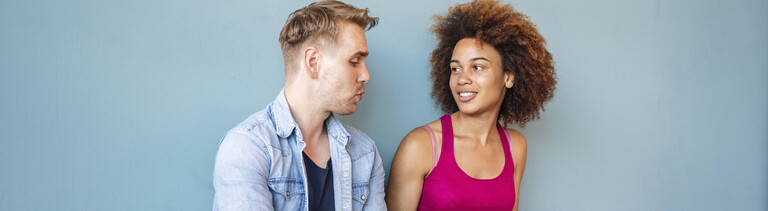 Ein Mann und eine Frau sitzen auf dem Boden. Auf den Beinen der Frau ist ein Laptop. Der Mann erzählt.