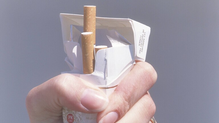 Eine Hand, die eine Packung Zigaretten zerquetscht.