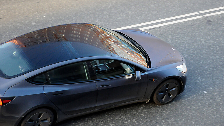 Ein schwarz-graues Auto der Marke Tesla fährt auf einer Straße. Das Bild zeigt das Auto von oben.