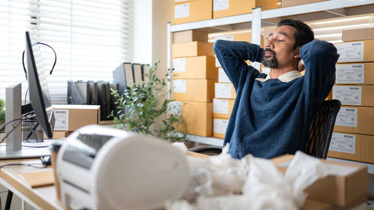 Gestresster Lagerarbeiter am Rechner, im Vordergrund zerknüllte Rechnungen