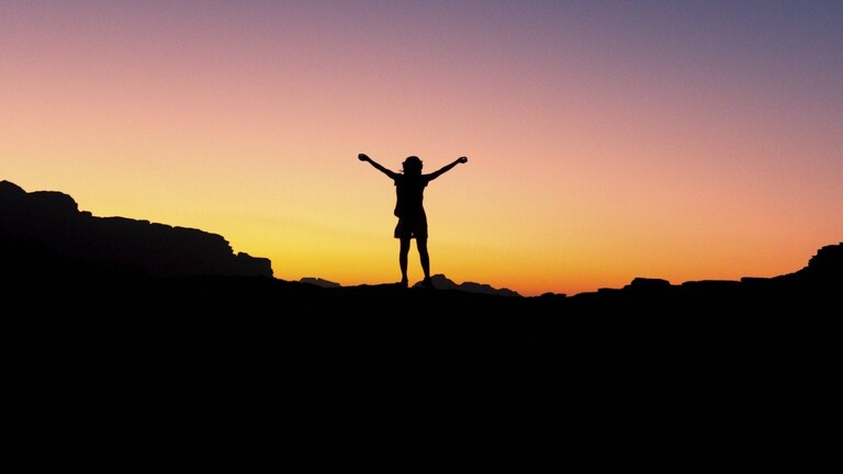 rau bei Sonnenuntergang oder Sonnenaufgang, die begeistert mit erhobenen Armen steht.