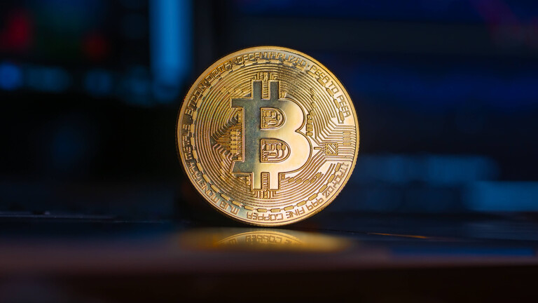 Eine goldene Bitcoin-Münze steht aufrecht vor einem Computer-Bildschirm.