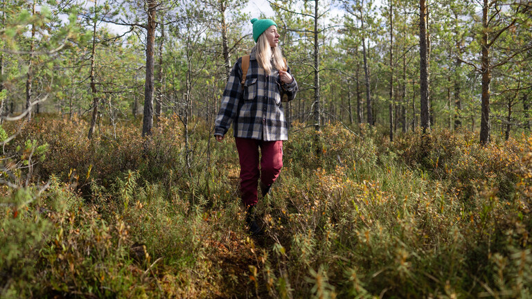 Eine Frau läuft in Wanderkleidung durch einen Wald.
