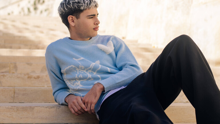 Ein junge Mann sitzt auf einer Treppe mit ausgestreckten Beinen und blickt in die Ferne (Symbolbild)