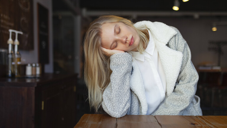 Foto einer jungen Frau, die den Kopf seitlich auf ihre Hand stützt und die Augen geschlossen hat