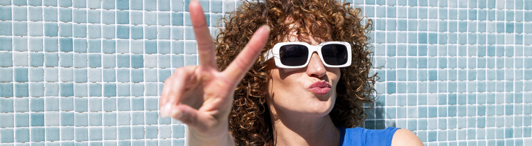 Frau mit Sonnerbrille macht Kussmund und Peace-Zeichen