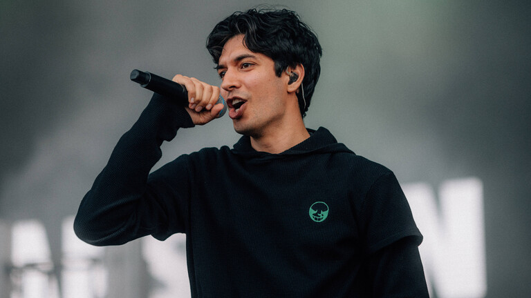 Der Berliner Rapper Apsilon steht in einem schwarzen Hoodie auf einer Festival-Bühne und hält das Mikrofon vor seinen Mund.