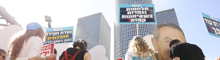 Teilnehmer einer Demonstration gedenken dem 7. Oktober 2023 tausend Tage, nachdem der Anschlag durch die Hammas verübt wurde. Die Menschen stehen vor einer Skyline in Tel Aviv und halten Schilder in die Luft (Tel Aviv, Israel, 2.07.2026)