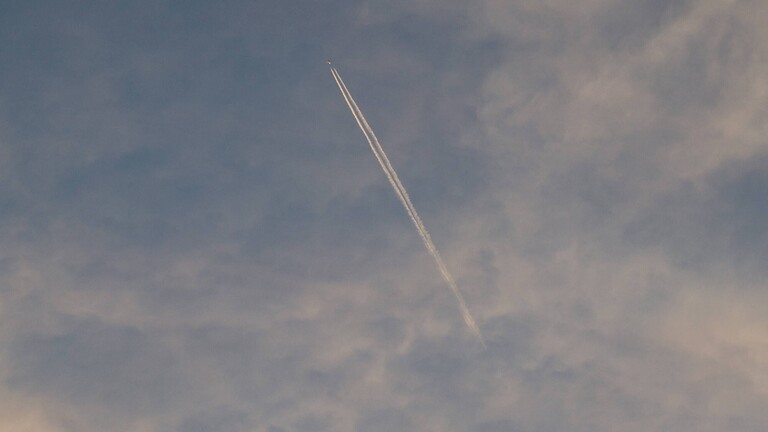 Ein Flugzeug hinterlässt einen Kondensstreifen am Himmel, der mit Schleierwolken bedeckt ist.