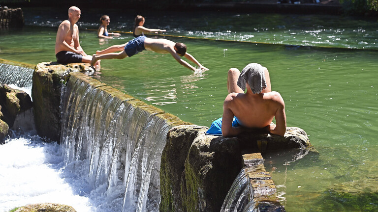Menschen suchen Abkuehlung im Eisbach in Muenchen.