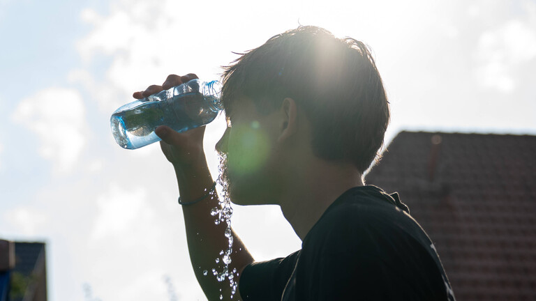 Ein junger Mann kühlt sich an einem heißen Sommertag mit Wasser ab.