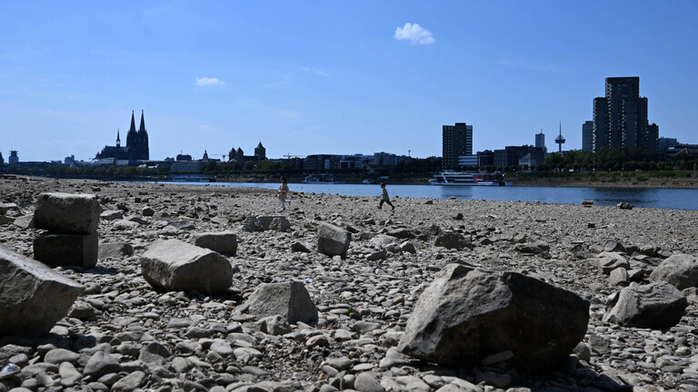 Der Rhein mit Niedrigwasser bei Köln Mülheim: Kinder spielen am ausgetrockneten Rheinufer, der Fluss selbst ist nur ein schmales blaues Band, im Hintergrund ist der Kölner Dom.