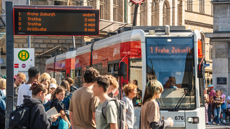 Menschen gehen an der Haltestelle Marktplatz vorbei, an der die Straßenbahn Linie 1 in Richtung Frohe Zukunft hält (Halle, 27.08.2026)