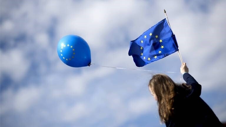 Eine junge Frau hält eine EU-Flagge und einen EU-Luftballon in der Hand