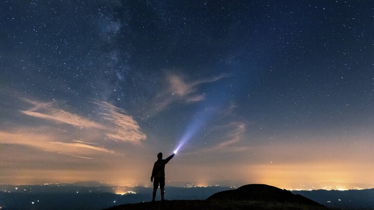 Mann leuchtet mit einer Taschenlampe in den Nachthimmel