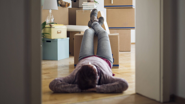 Eine Frau legt Pause bei ihrem Umzug ein. Sie liegt am Boden und hat die Beine auf einen Umzugskarton gelegt.