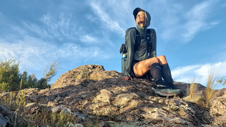 Eine Frau in Wanderkleidung blickt auf einem Felsen in die Sonne
