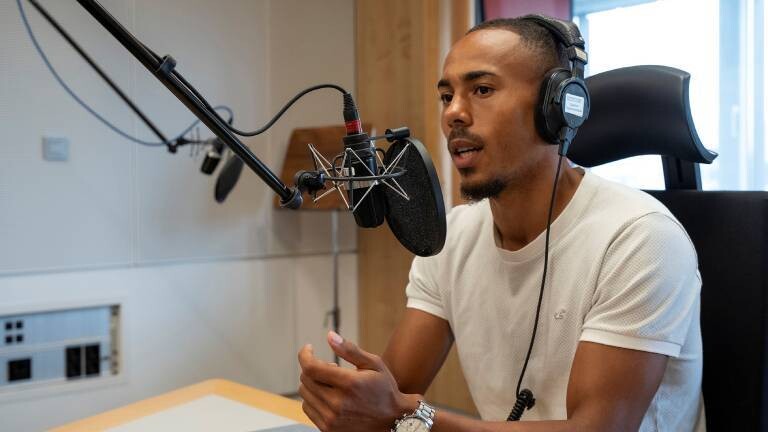 Der Fußballspieler Robin Afamefuna sitzt im Dlf Nova-Studio am Mikrofon und hat einen Kopfhörer auf.