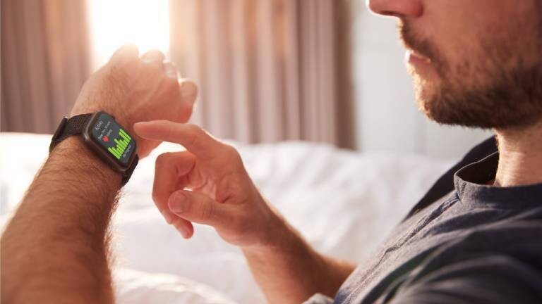 Ein junger Mann kontrolliert im Bett seinen Schlaftracker.