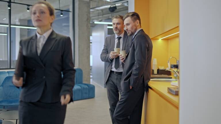 Zwei Männer schauen einer Arbeitskollegin lüstern hinterher