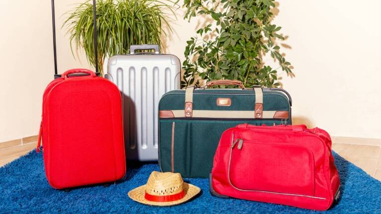 Vier Gepäckstücke stehen gepackt zum Urlaubsbeginn auf einem blauen Teppich.