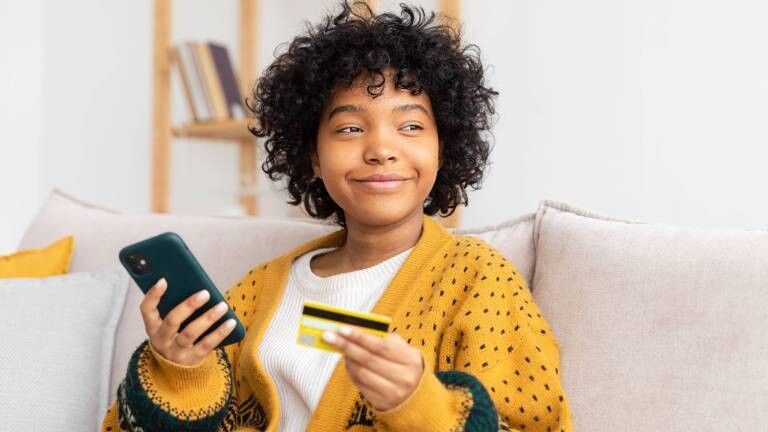 Frau hält in der rechten Hand ihr Smartphone und mit der linken Hand eine goldene Kreditkarte während des Online-Shoppings.