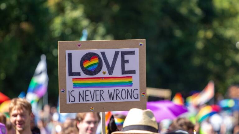 Auf einer Kundgebung der queeren Community halten in Ostdeutschland Teilnehmende ein Schild mit der Aufschrift "LOVE IS NEVER WRONG" hoch.