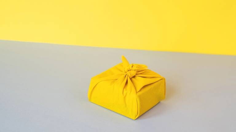 Geschenk in gelbem Furoshiki-Seidenpapier in Japan eingewickelt.