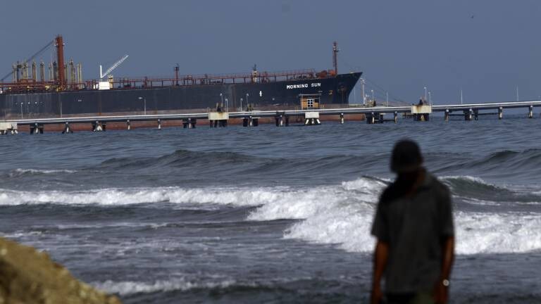 Ein Mann spaziert am Strand von El Palito entlang, im Hintergrund ist die Raffinerie zu sehen, der unter panamaischer Flagge fahrende Öltanker Morning Sun am Dock der Raffinerie El Palito in Puerto Cabello, Bundesstaat Carabobo.