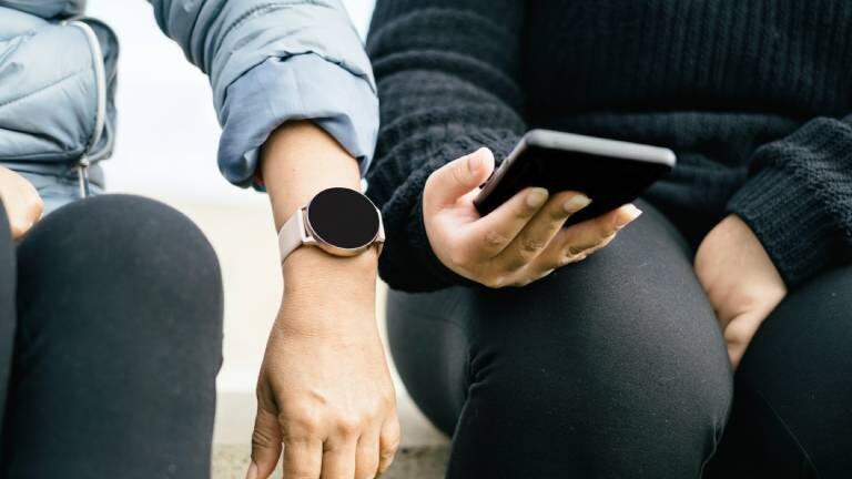 Zwei Frauen tragen Smartphone/Smartwatch und gucken auf die Geräte.