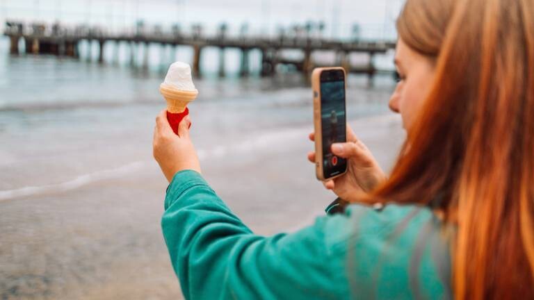 Nahaufnahme einer Frau mit Eis, die am Strand von Danzig ein Selfie macht.